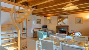 Amplia sala de estar con una escalera de madera, chimenea y una mesa de comedor lista para una comida.