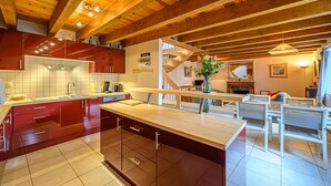 Una cocina moderna con gabinetes rojos, una isla de madera y un comedor con sillas blancas.
