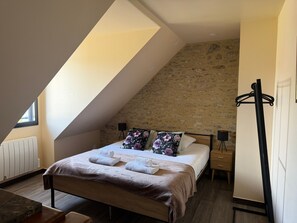 A bedroom with a sloped ceiling, a bed with a brown headboard, a bedside table, a lamp, and a coat rack.
