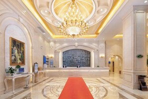 Un vestíbulo de hotel con alfombra roja, un candelabro y un mural grande en la pared.