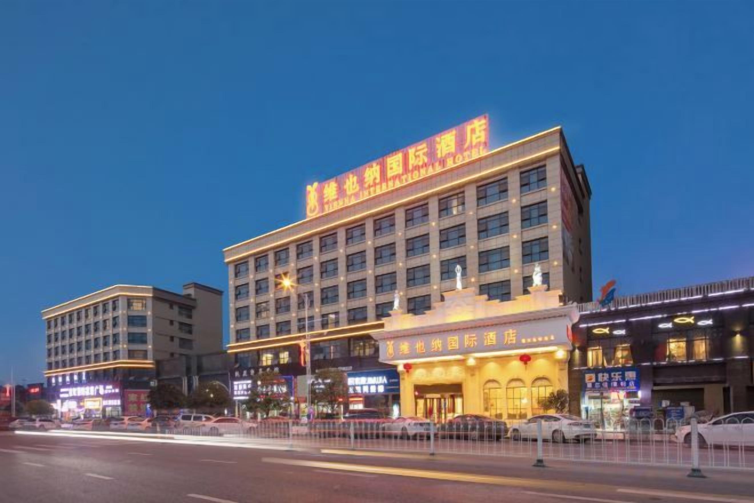 A multi-story hotel with a prominent sign, multiple ground-level shops, and a well-lit facade.