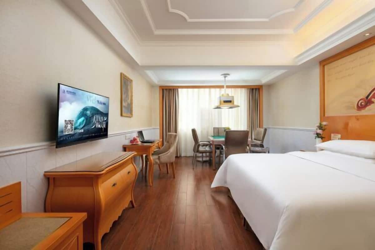 A hotel room with a bed, a desk, a chair, a television, and a window with curtains.