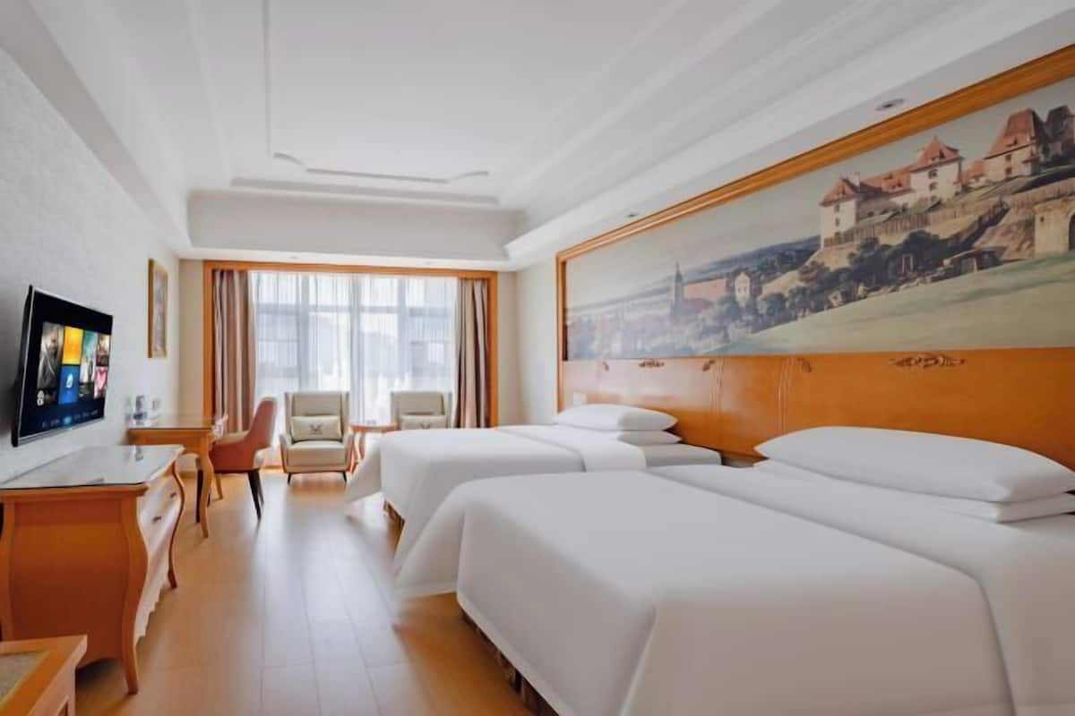 A hotel room with two beds, a desk with a TV, a chair, and a painting on the wall.