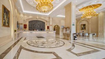 A spacious lobby with a marble floor, a reception desk, and a chandelier.