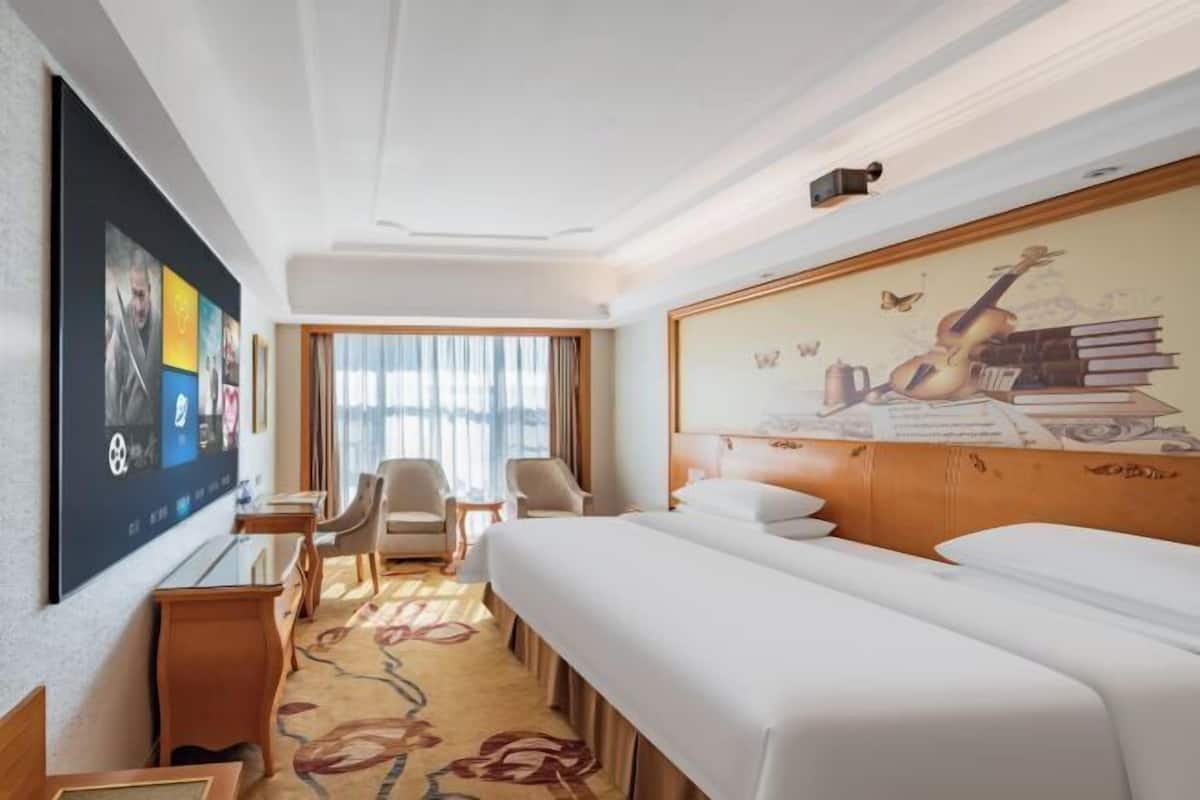 A hotel room with a large bed, two chairs, a desk, and a TV mounted on the wall.