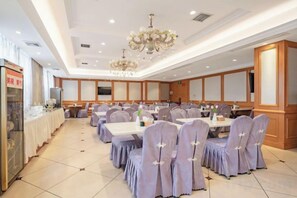 Un salón de banquetes con mesas redondas, sillas y una araña.