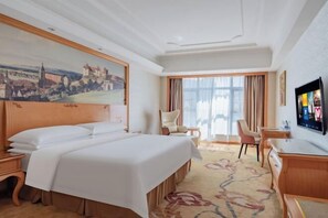 A hotel room with a large bed, a desk, a chair, a television, and a painting on the wall. - Vienna Hotel (Longhui High-speed Railway Station) (Longhui)