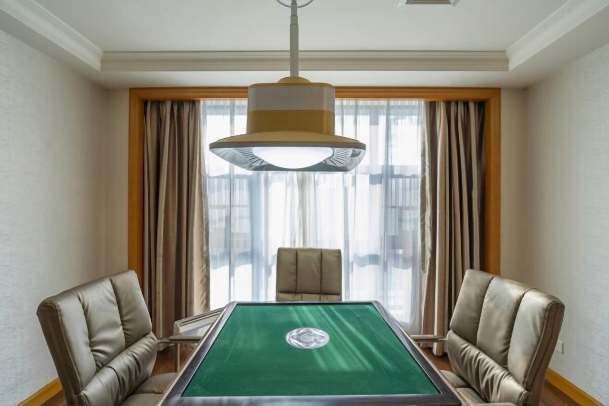 A conference room with a green table, leather chairs, and a large hanging lamp.