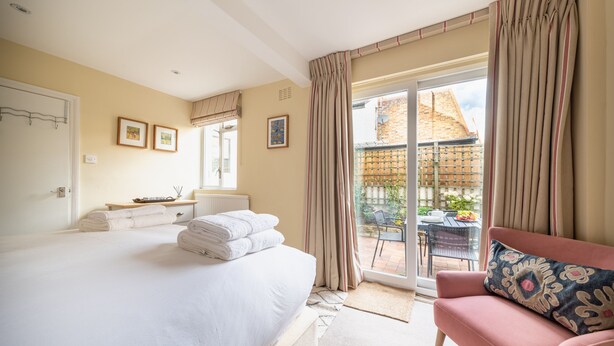 Ein Schlafzimmer mit einem großen Bett, einem pinken Sessel und einem Balkon mit Blick auf Gebäude.