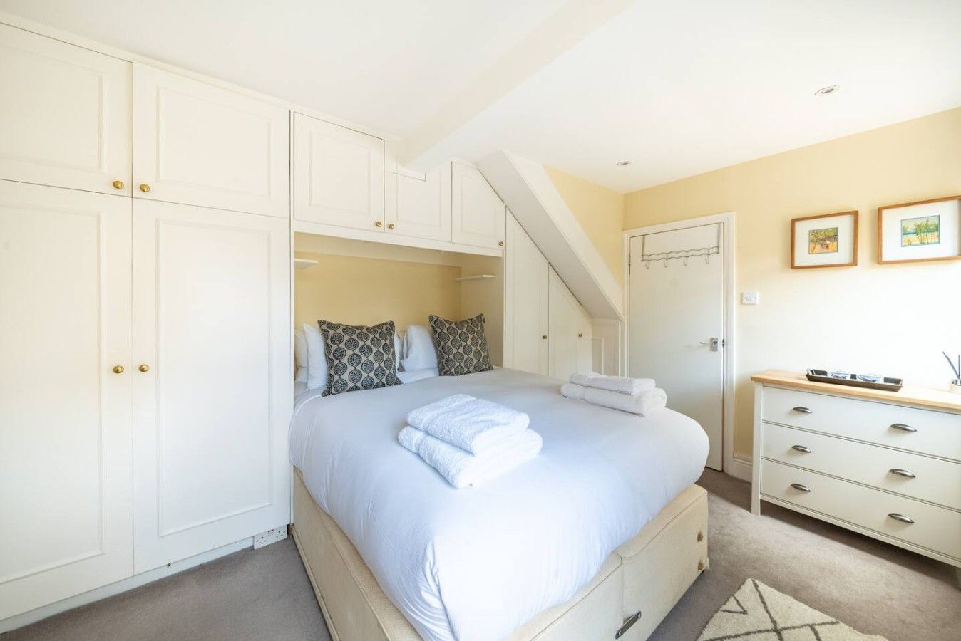 A bedroom with a bed, a chest of drawers, a wardrobe, and a staircase.