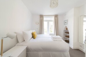 A hotel room with a bed, bedside table, lamp, and a view of the outdoors. - Elegant 2-bed Fulham house with private garden (London)