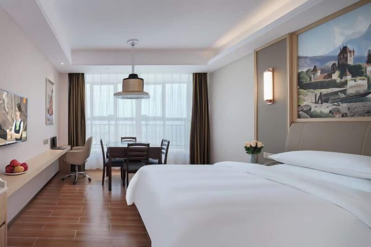 A hotel room with a bed, desk, chair, and a painting on the wall.