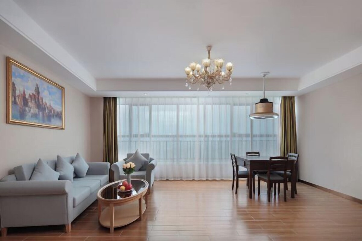 Ein Wohnzimmer mit Sofa, Couchtisch, Esstisch, einer Kandelaber und einem großen Fenster mit Vorhängen.