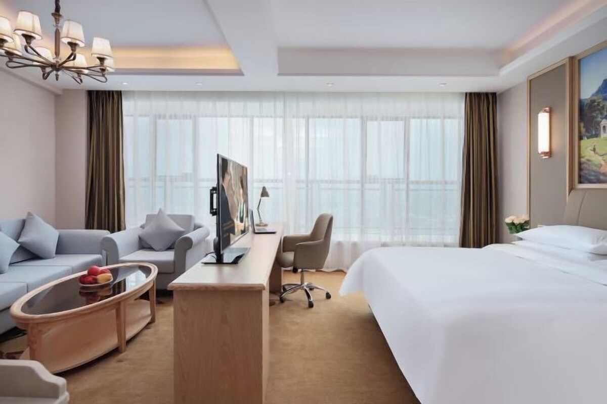 Ein Hotelzimmer mit einem großen Bett, einer Couch, einem Schreibtisch mit Computer und einem Fernseher.