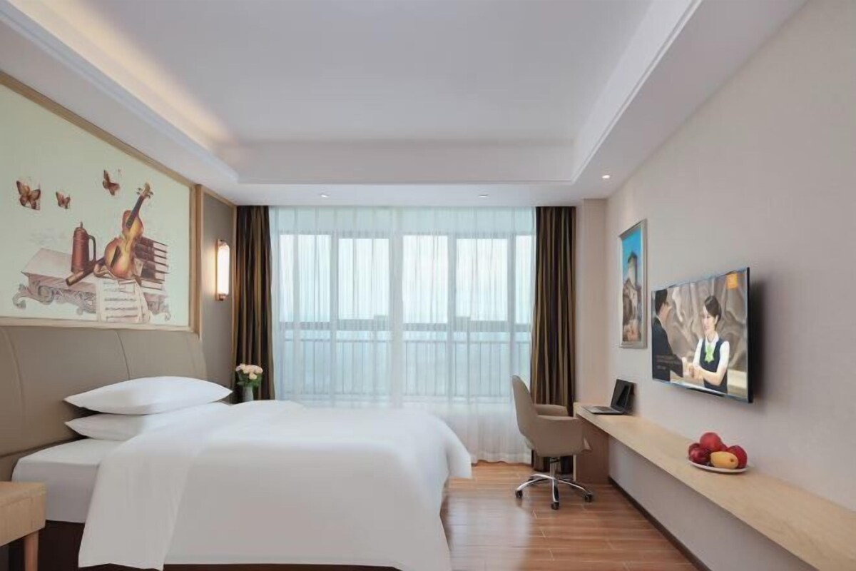 Ein Hotelzimmer mit Bett, Schreibtisch, Stuhl, Fernseher und einem Fenster mit Vorhängen.
