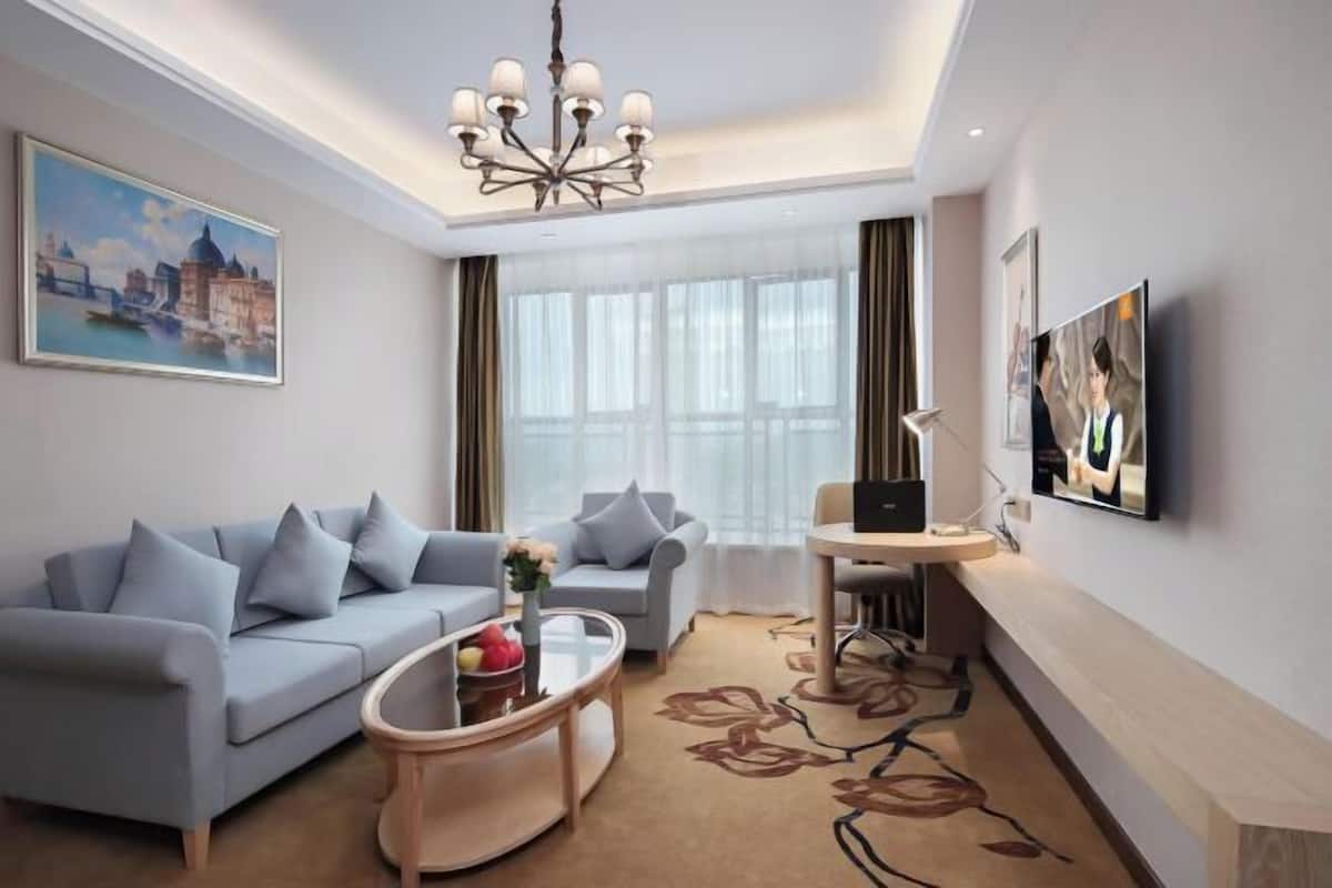 A modern hotel room with a sofa, armchair, coffee table, TV, and artwork.