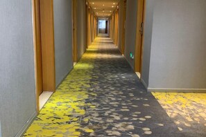 A hotel corridor with a patterned carpet, wooden doors, and a view into the distance. - Yiru Hotel (Xinfeng) (Xinfeng)