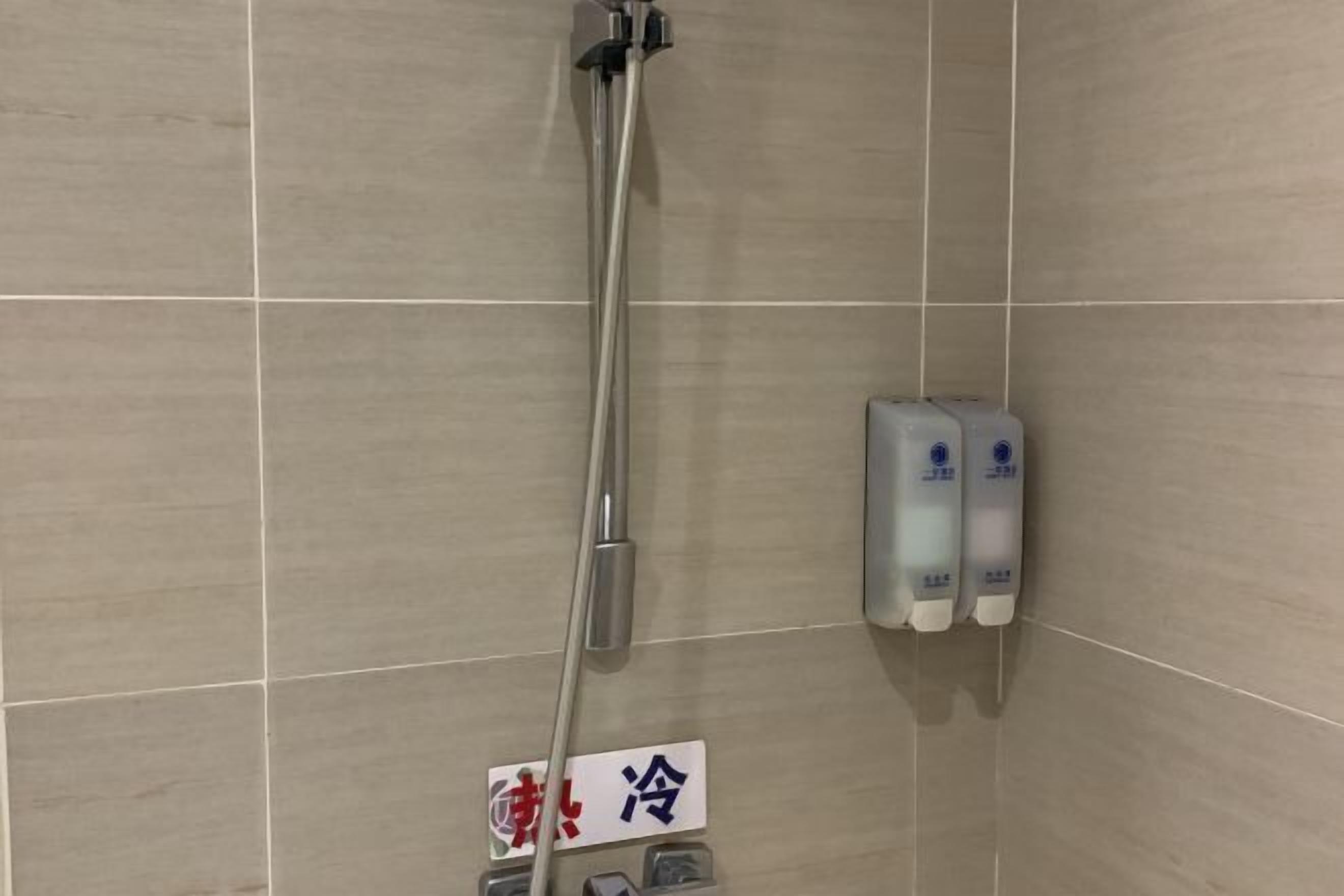 Un espace douche avec un mur carrelé, une pomme de douche et deux distributeurs de savon.
