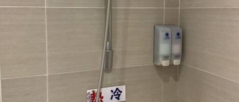 Un espace douche avec un mur carrelé, une pomme de douche et deux distributeurs de savon.