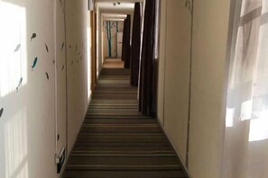 A hotel corridor with a striped carpet, doors on both sides, and a window on the right. - Yiru Hotel (Xinfeng) (Xinfeng)