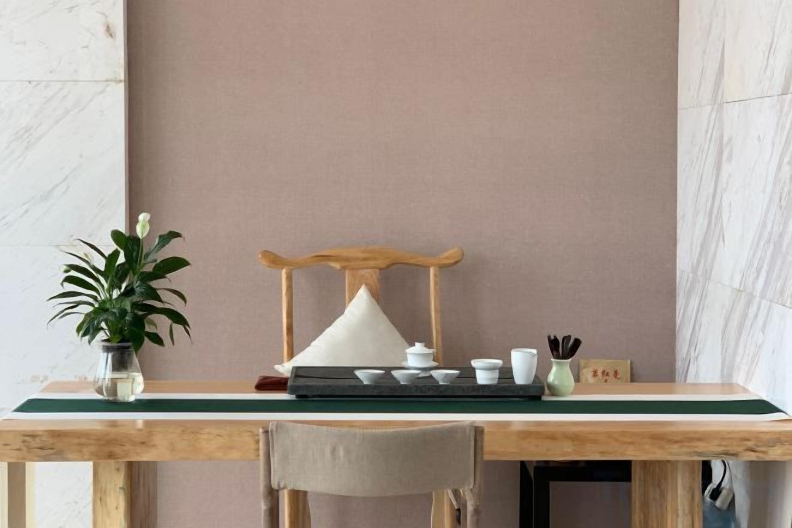 Una mesa de madera con un mantel verde, una silla, una planta en maceta, otra silla de madera y una mesita con tazas y una tetera.