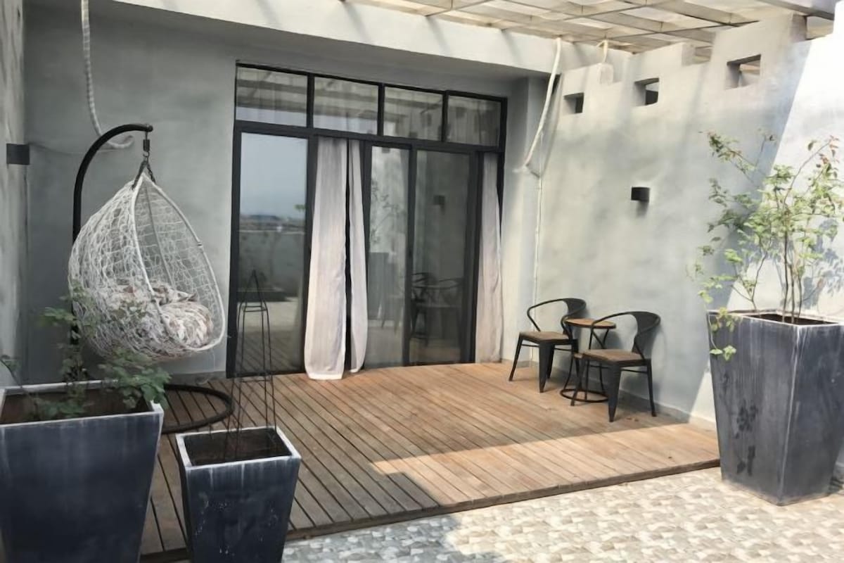 A wooden deck with a hanging chair, two chairs, and potted plants.