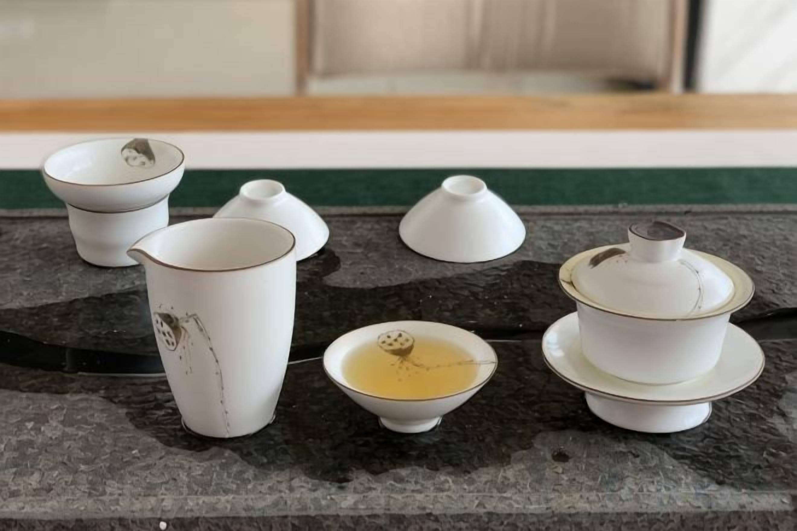 A set of white ceramic tea cups and teapots on a granite countertop.