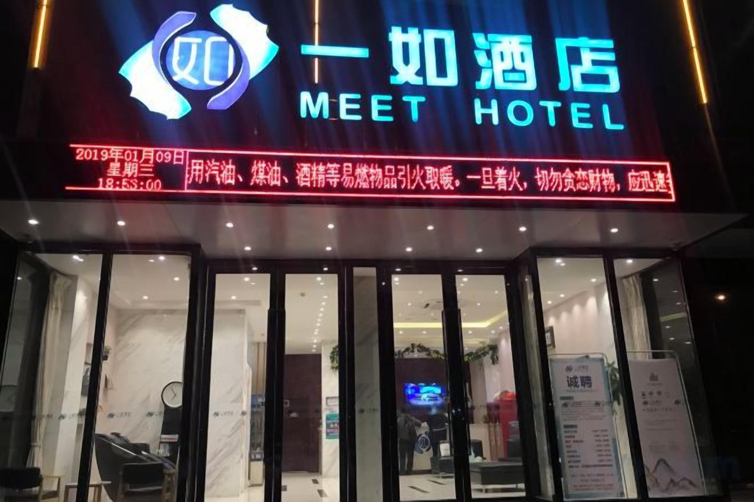 A hotel entrance with a neon sign, glass doors, and a reception area visible inside.