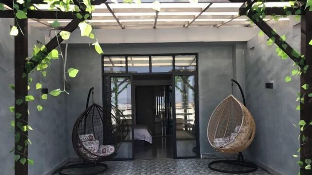 A covered patio with two hanging chairs, a tiled floor, and a glass door leading to an interior space. - Yiru Hotel (Xinfeng) (Xinfeng)