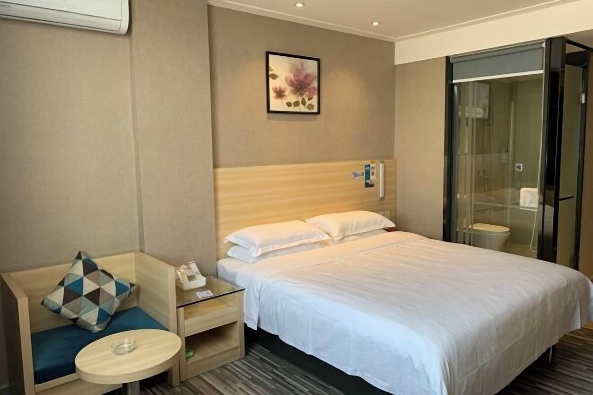 A hotel room with a bed, a seating area with a table, a shower, and a framed picture on the wall.