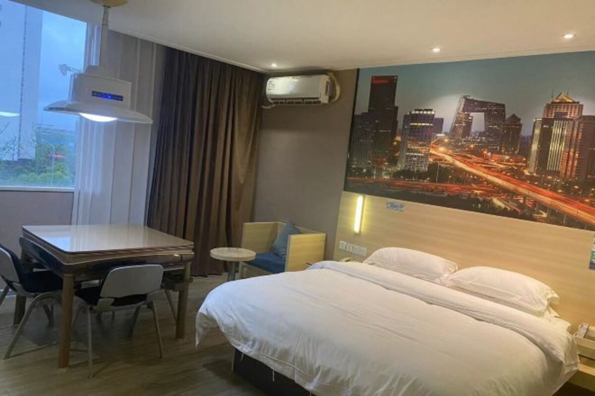 A hotel room with a bed, a desk, a chair, an air conditioner, and a cityscape mural on the wall.