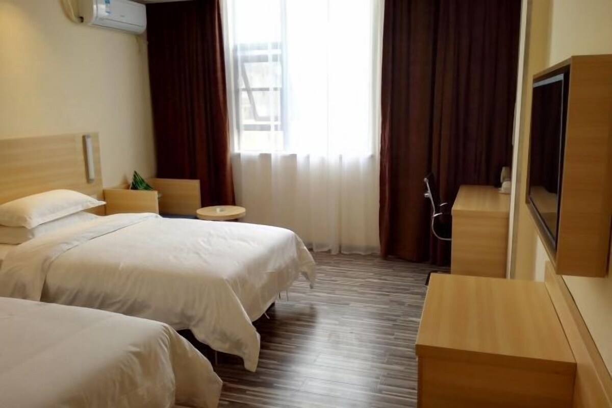 A hotel room with two beds, a small round table, a TV, and a wooden floor.
