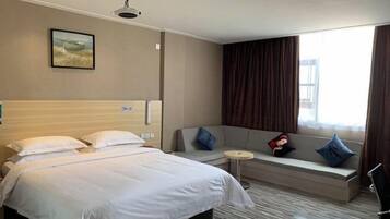 A hotel room with a bed, a sofa, a small round table, and a window with curtains.