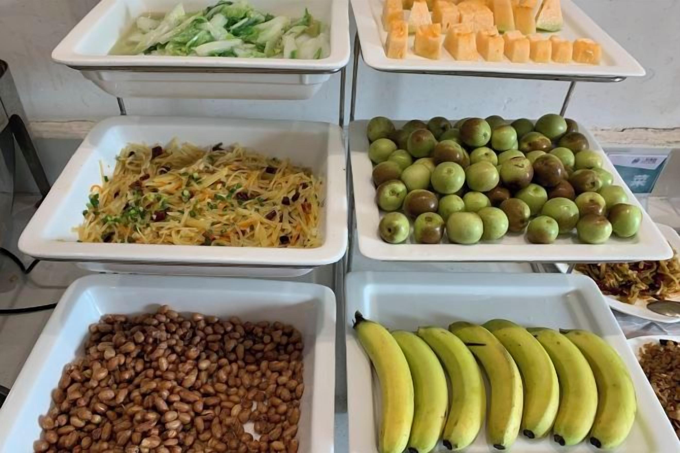 A buffet with various food items including pasta, apples, bananas, and nuts.