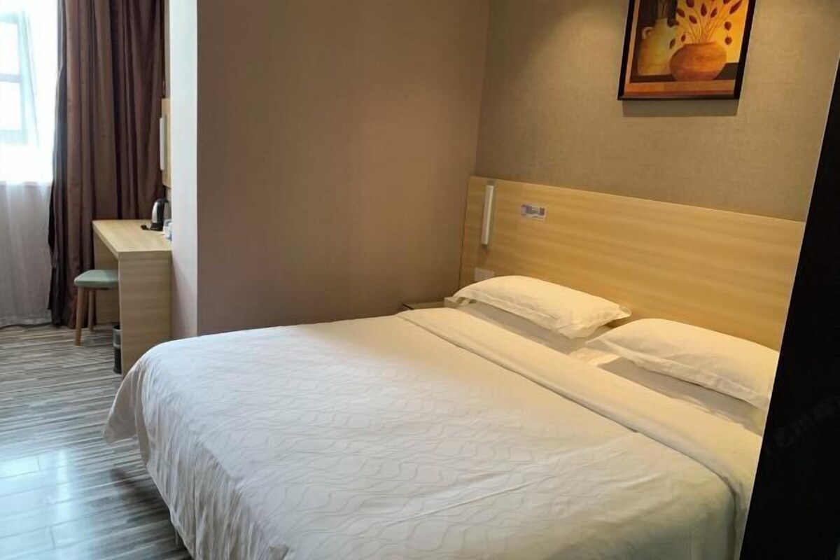 A hotel room with a bed, a desk, and a painting on the wall.