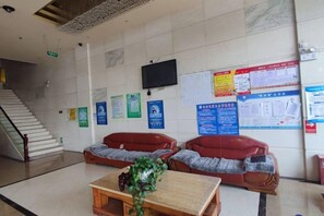 A lobby with a staircase, red leather sofas, a wooden table with a plant, and informational posters on the walls. - San Xinle Grand Large Hotel (Wenshan City)