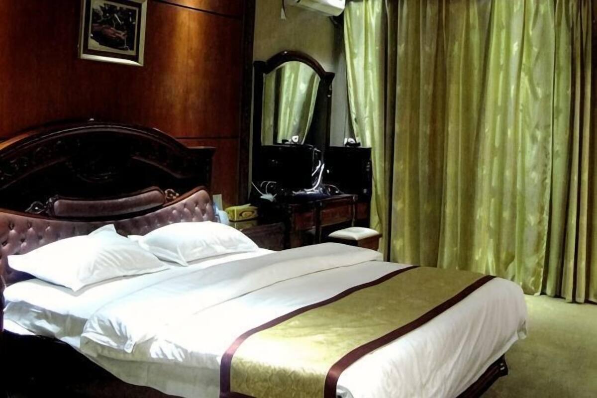 Un lit bien fait, avec une tête de lit, une table de chevet avec une lampe et un miroir au mur.