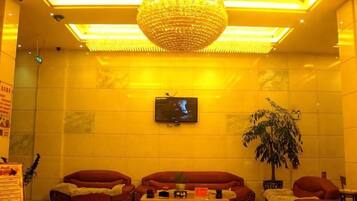 A lobby with a television mounted on the wall, a large chandelier, and seating arrangements.