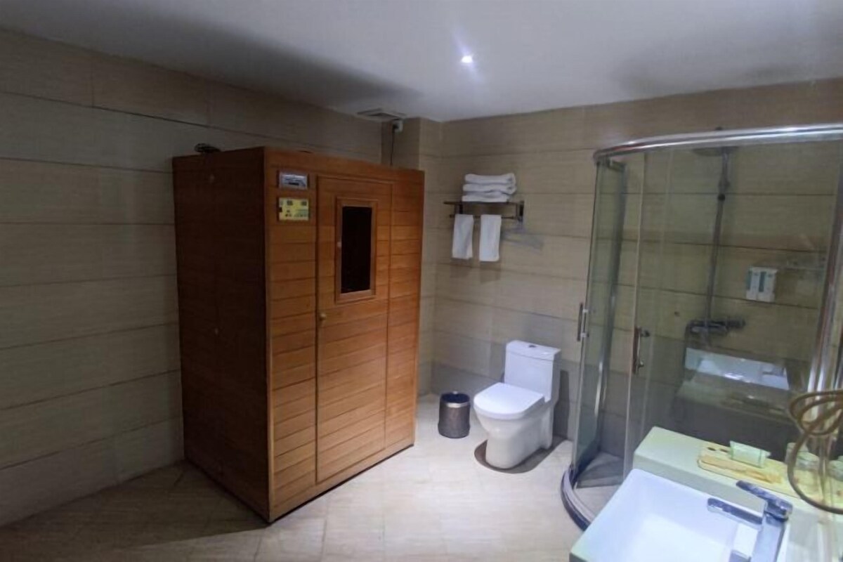 A bathroom with a wooden cabinet, a toilet, a glass shower enclosure, and a sink with toiletries.
