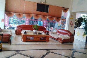 A lobby with leather sofas, a wooden coffee table, and a large window with a view of buildings.