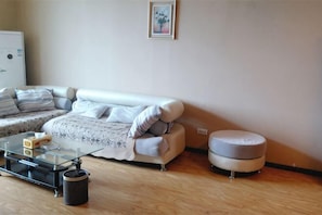 A living room with a sofa, ottoman, glass coffee table, and a trash can. - San Xinle Grand Large Hotel (Wenshan City)