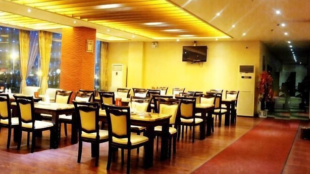 Un restaurante con varias mesas y sillas, un televisor en la pared y una alfombra roja que lleva a la entrada.