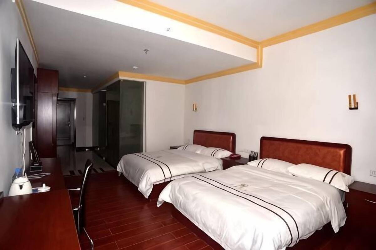 Une chambre d’hôtel avec deux lits, un bureau, une télévision et une salle de bain visible à travers une porte ouverte.