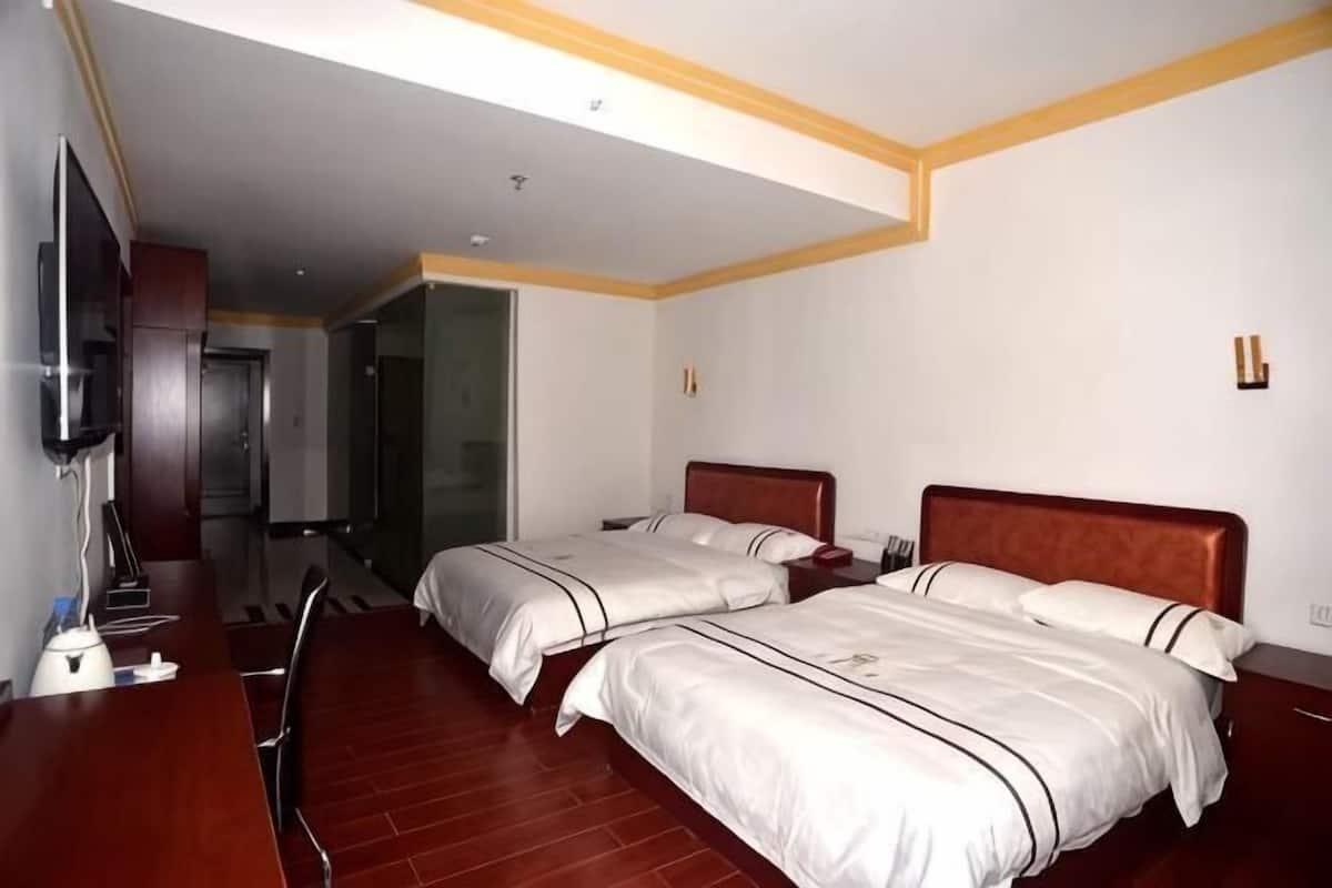 A hotel room with two beds, a desk, a TV, and a bathroom visible through an open door.