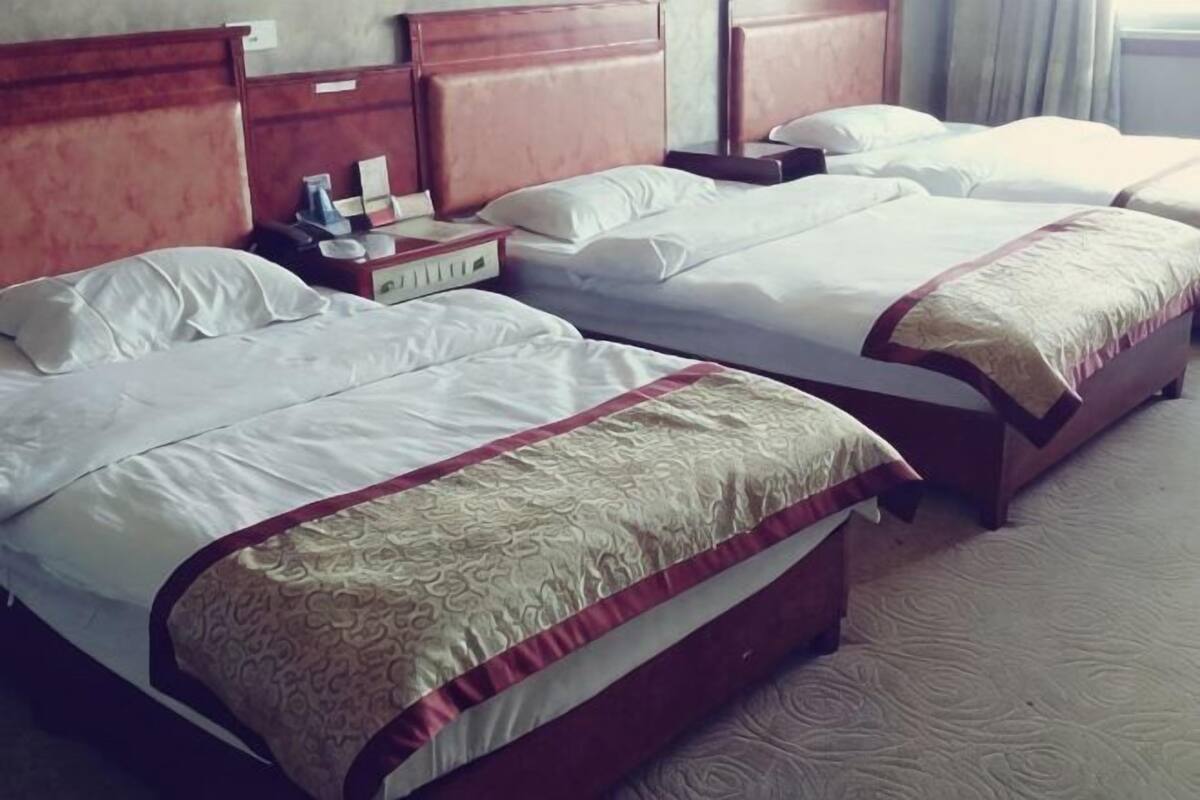 Une chambre d’hôtel avec trois lits, des têtes de lit en bois et une table de chevet avec une lampe.