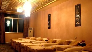 Una habitación con varias camillas de masoterapia alineadas, un ventanal con cortinas y un equipo de aire acondicionado instalado en la pared.