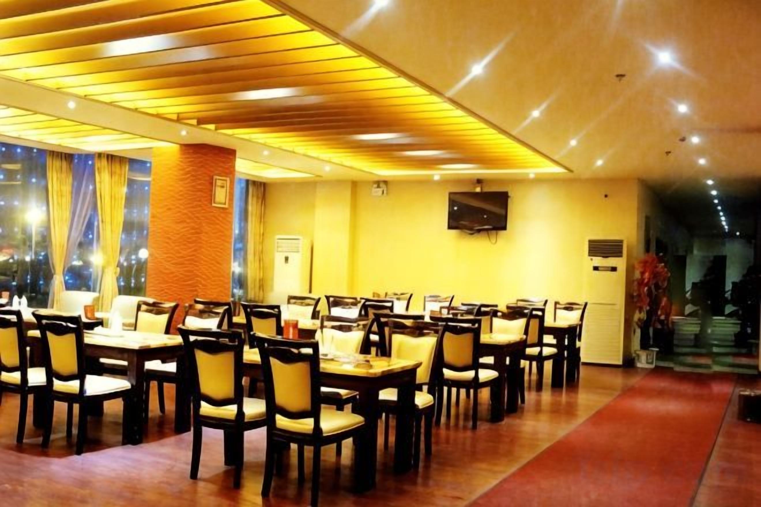 A dining area with multiple tables and chairs, a television mounted on the wall, and a red carpet leading to the exit.