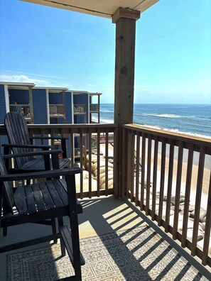 A wooden deck with a view of the ocean, a chair, and a building with multiple windows.