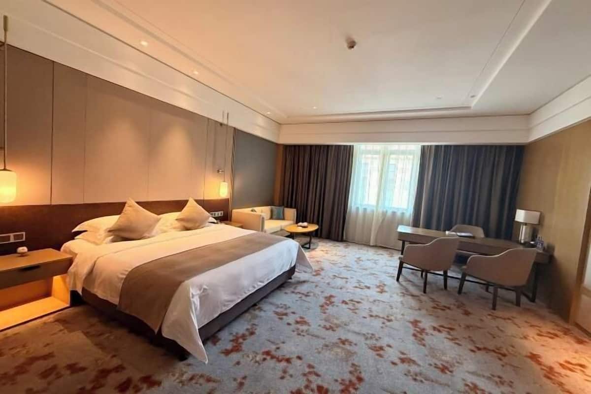 Une chambre d’hôtel avec un grand lit, des tables de chevet, un bureau, des chaises et une vue sur l’extérieur.