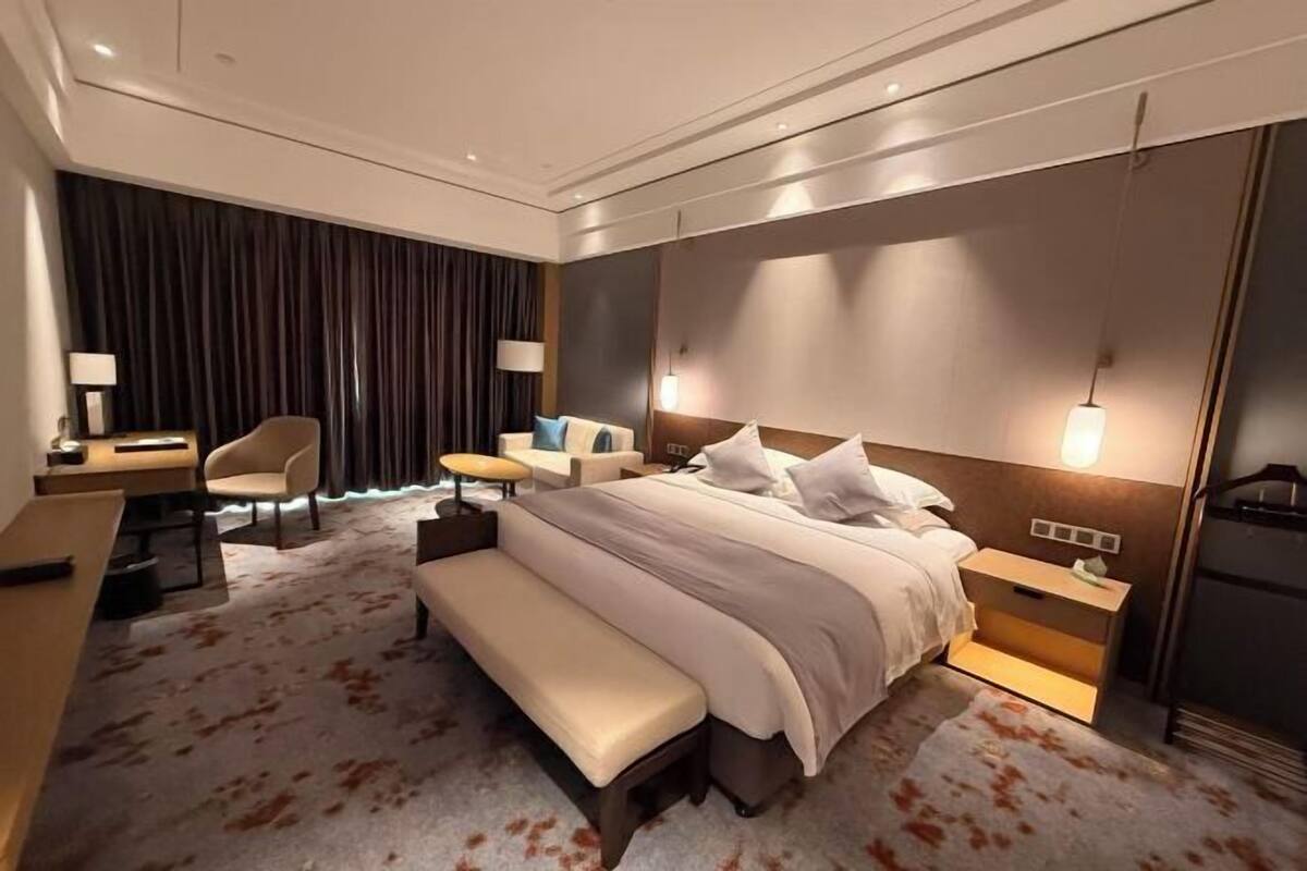 Une chambre d’hôtel moderne, dotée d’un grand lit, d’un bureau, d’une chaise, d’un banc et d’une petite table.